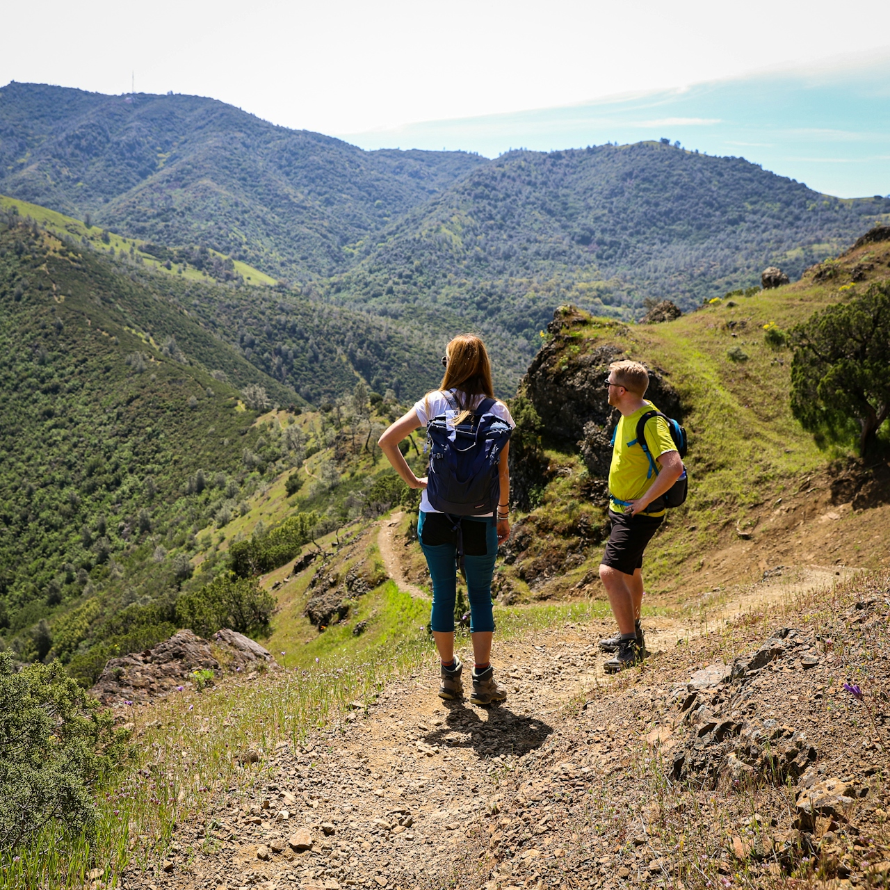 Two hikers are taking in the view of mountains and green rolling hills on a trail at Mount Diablo State Park 